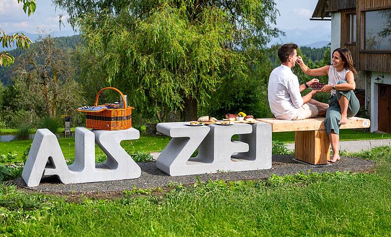 Pärchen sitzt mit einem Picknickkorb auf der Zeitbank beim Natur Gut Lassen