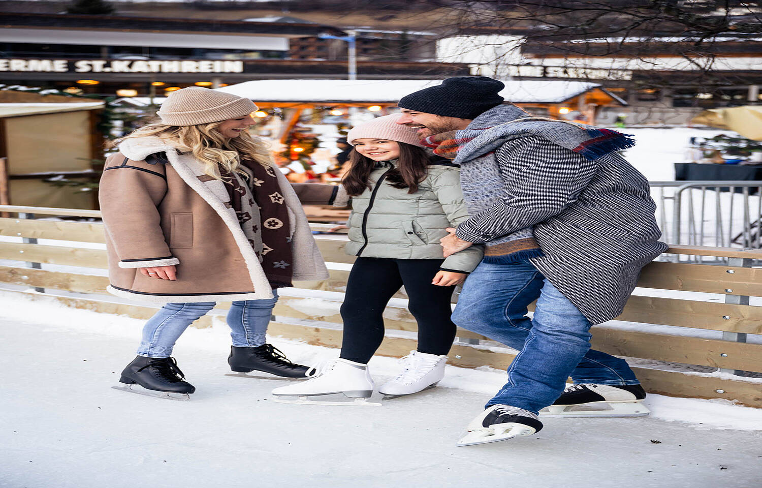 Mutter, Vater & Kind stehen auf dem Eislaufplatz und haben Spaß
