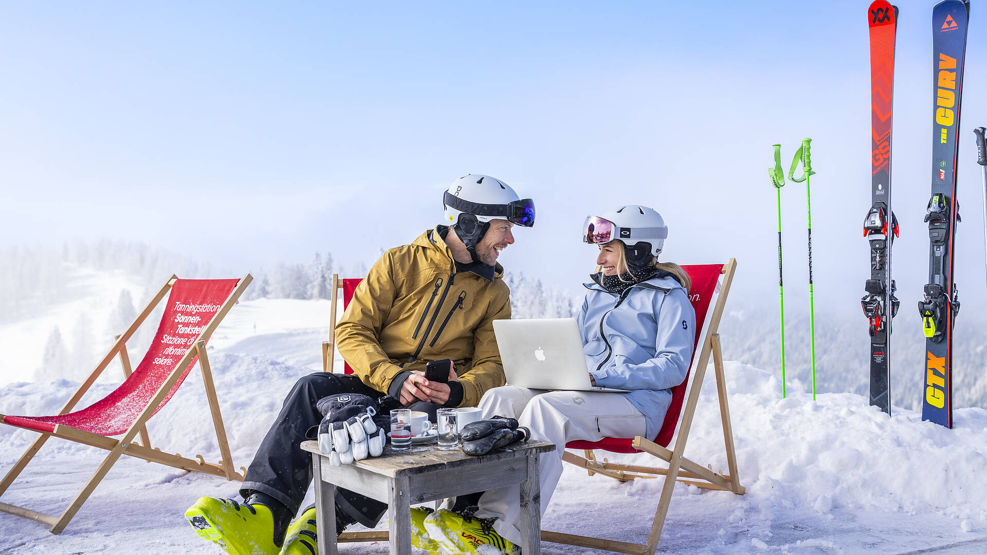 2 Personen sitzen in Liegestühlen auf Skipiste mit Laptop