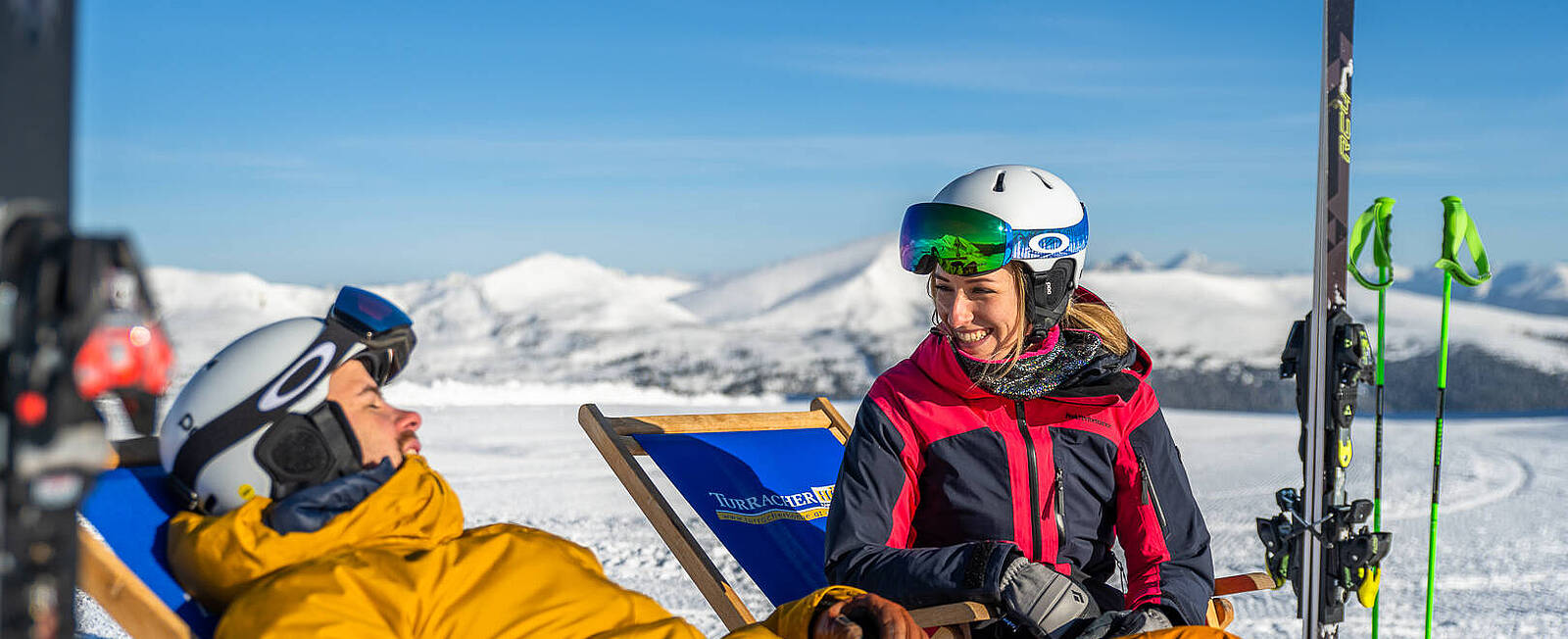 2 Personen sitzen in Liegestühlen, genießen die Sonne und haben Spaß miteinander