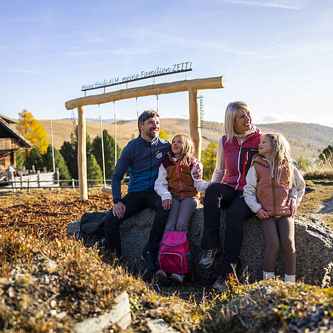 Familie sitzt am ZEITplatz in den Nockbergen und genießt bei einer Pause die Aussicht auf die Berge.