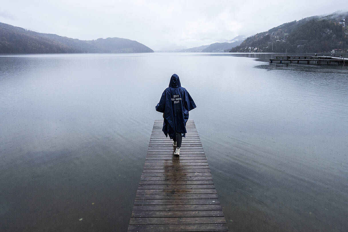 Person geht mit Regenponcho auf Steg