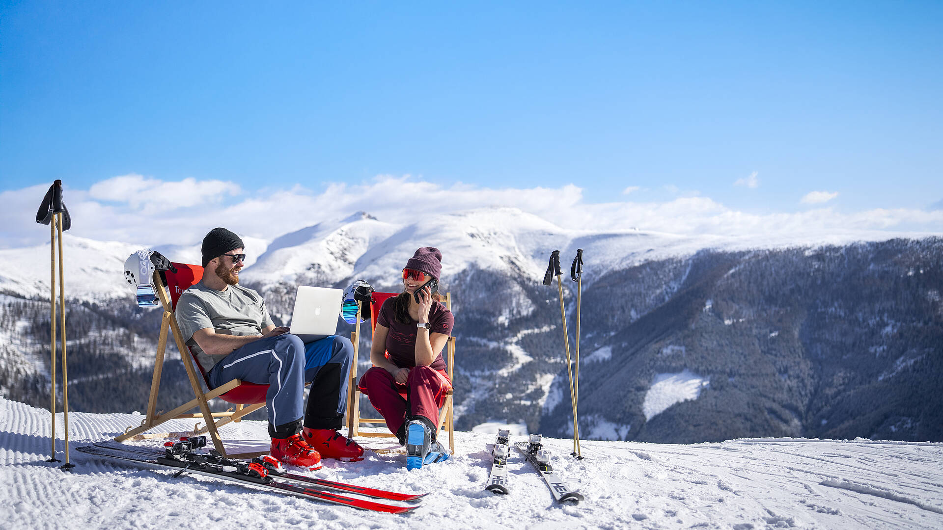 2 Personen sitzen in Liegestühlen auf der Skipiste und arbeiten mit ihre Smartphones