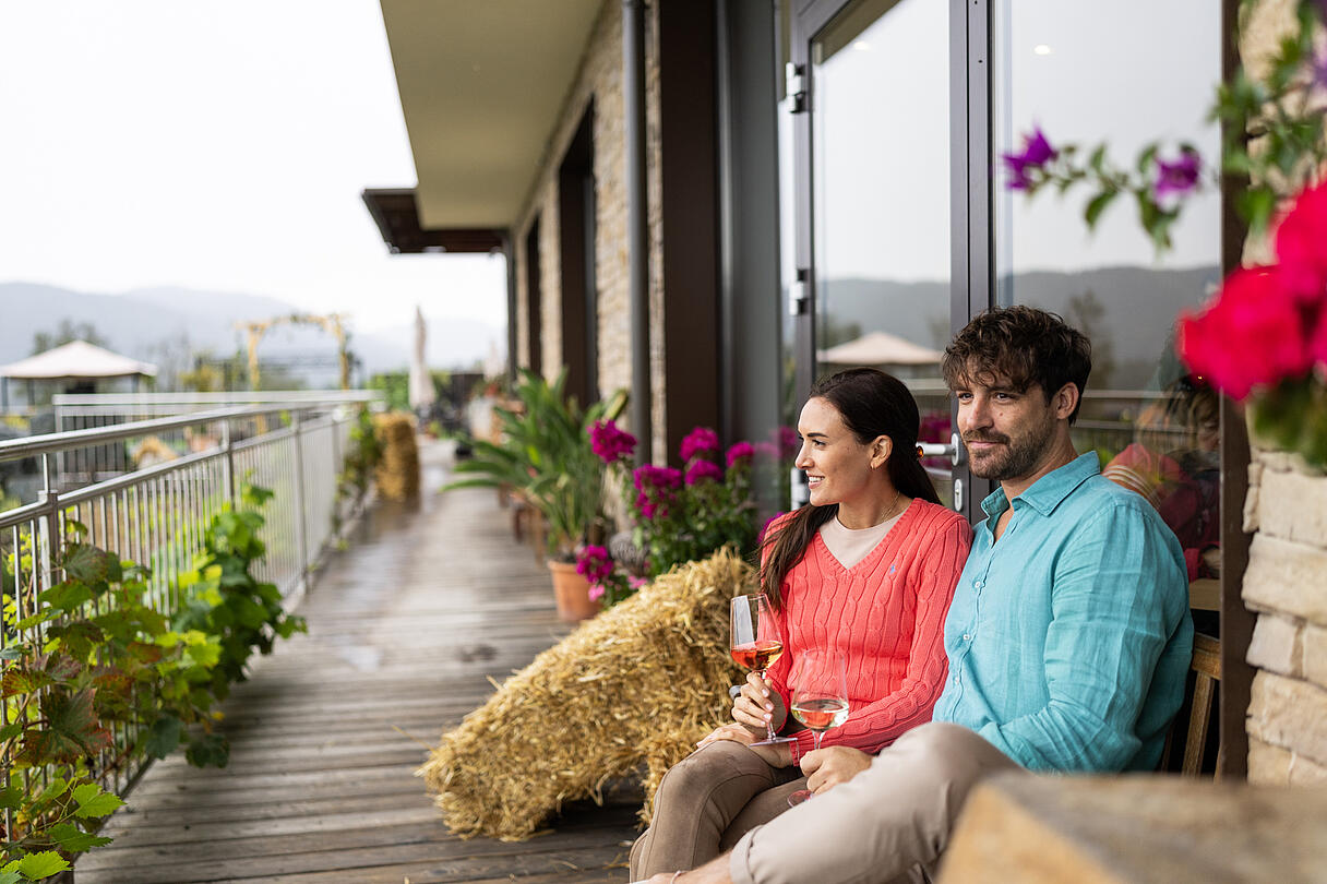 Pärchen sitzt im Herbst mit 2 Weingläsern in der Hand auf Terrasse beim Maltschacher See
