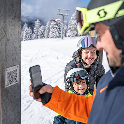 Familie mit Kind scannt QR-Code am ZEITplatz Alles in AlmZEIT auf der Hochrindl