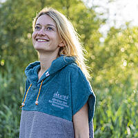 Junge Frau trägt Badeponcho in blau grau mit Logo auf der Brust
