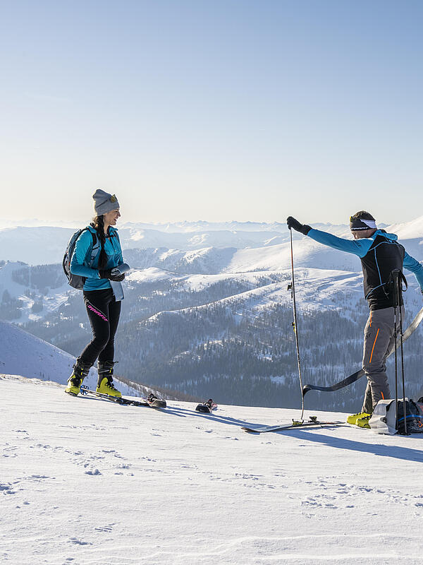 Skitourengeher ziehen am Gipfel ihre Skifelle ab Ein Mann und eine Frau stehen in den Bergen und der Mann zieht gerade die Felle von seinen Tourenskiern ab