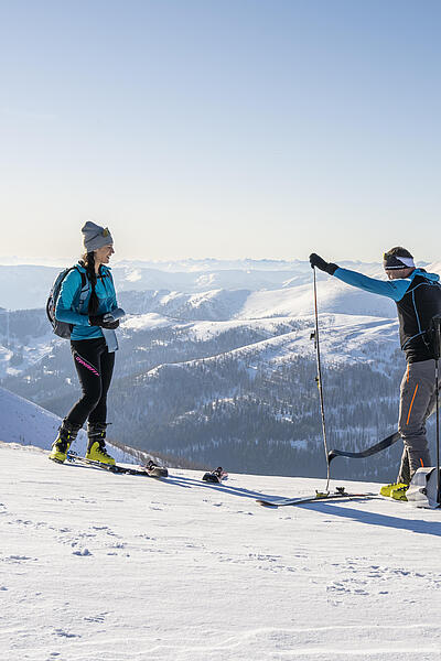 Skitourengeher ziehen am Gipfel ihre Skifelle ab Ein Mann und eine Frau stehen in den Bergen und der Mann zieht gerade die Felle von seinen Tourenskiern ab