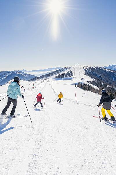 Familie fährt an einem sonnigen Tag eine breite Piste im Skigebiet Bad Kleinkirchheim hinunter