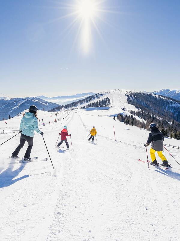 Familie fährt an einem sonnigen Tag eine breite Piste im Skigebiet Bad Kleinkirchheim hinunter