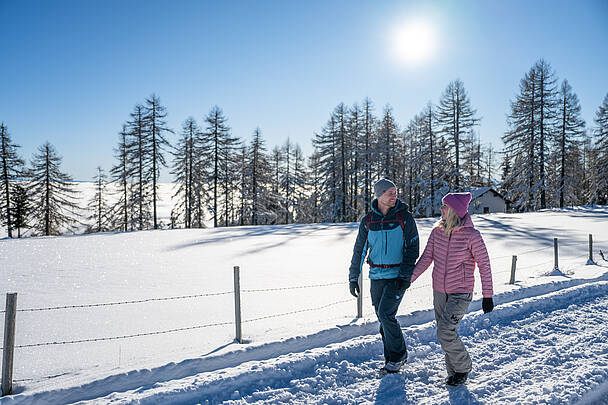 Paar beim Winterwandern auf präpariertem Weg in sonniger Schneelandschaft der Nockberge.