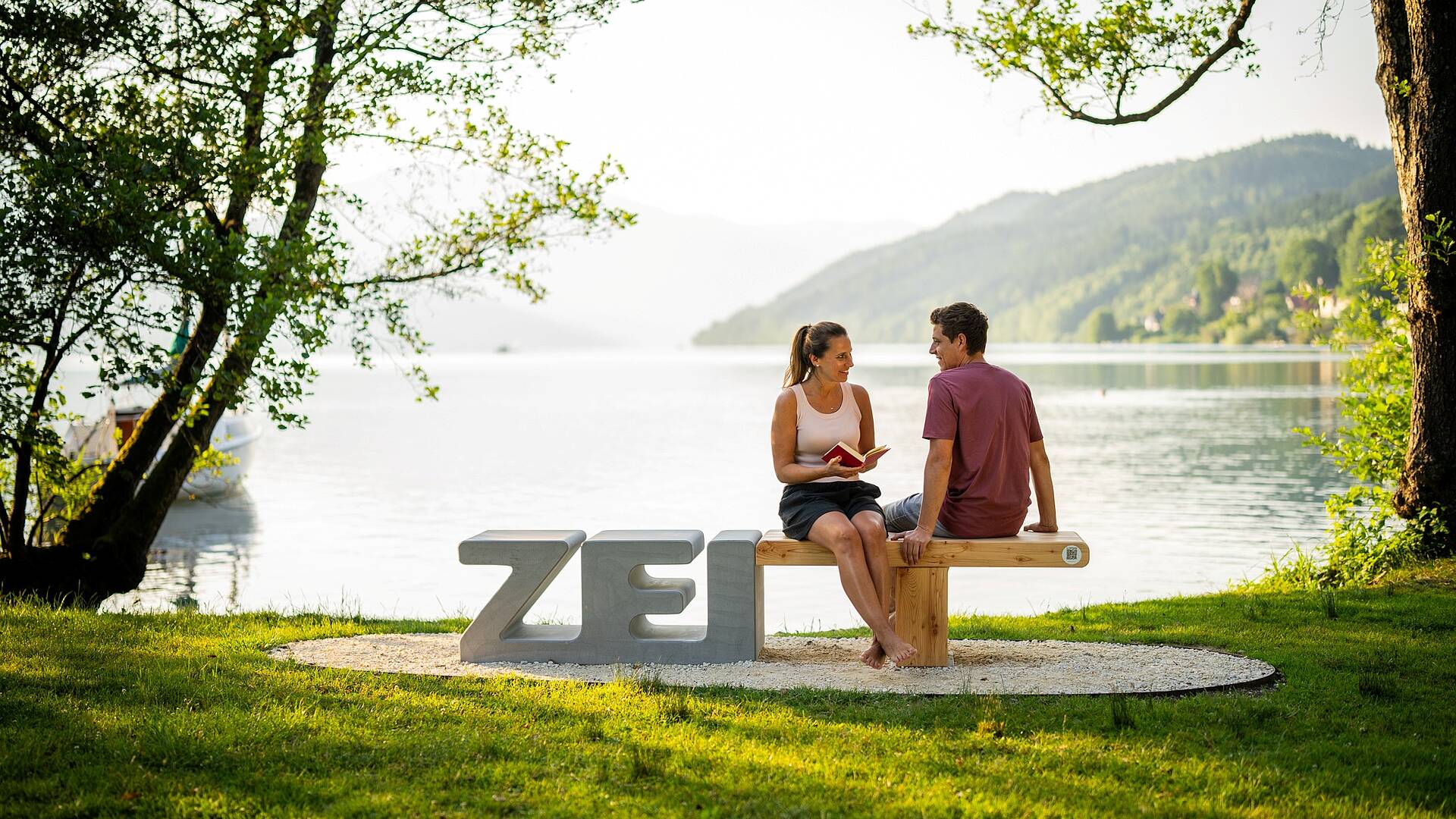Pärchen sitzt auf Zeitbank mit dem Millstätter See im Hintergrund