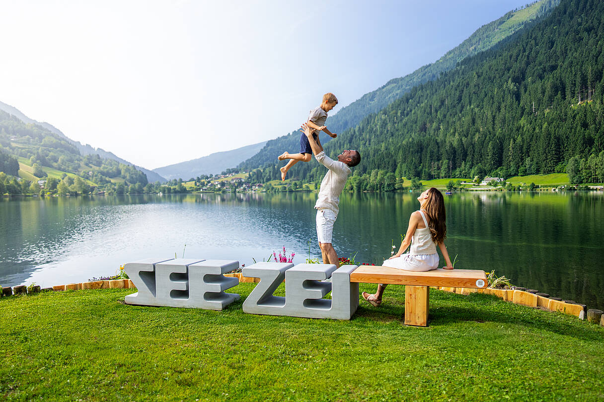 Familie bei der Zeitbank am Brennsee und Vater wirft das Kind in die Höhe und fängt es wieder