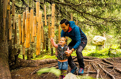 Ein Mann hilft seinem Kind die herabhängenden Hölzer im Naturbegegnungspark Silva Magica zu entdecken
