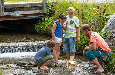 3 Kinder stehen im Bach und suchen etwas bei der Wassersafari