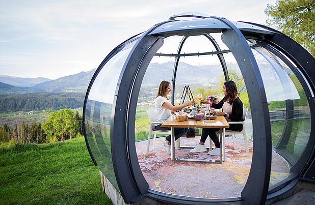 2 Personen sitzen in der Glaskuppel und genießen ihren Brunch an einem schönen Sommertag
