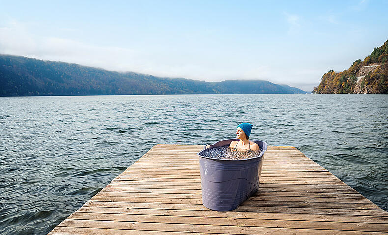 Frau liegt in Badewanne, die mit Eiswasser gefüllt ist, auf einem Holzsteg am Millstätter See