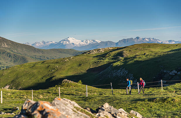 2 Personen wandern am Nockberge-Trail entlang mit einem atemberaubenden Bergpanorama