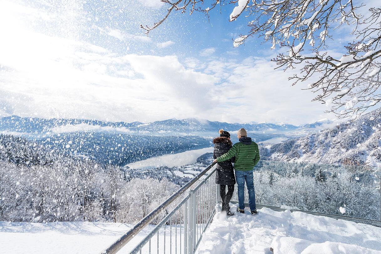 Pärchen stehth im Winter auf verschneitem Sternenbalkon mit Aussicht auf den Millstätter See