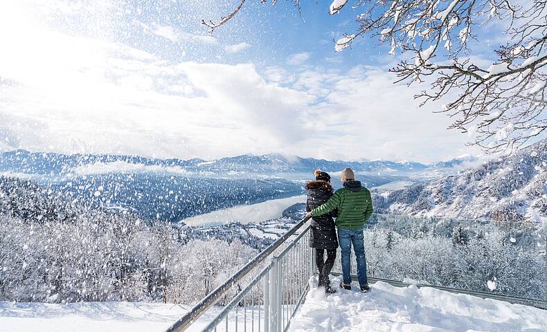 Pärchen stehth im Winter auf verschneitem Sternenbalkon mit Aussicht auf den Millstätter See