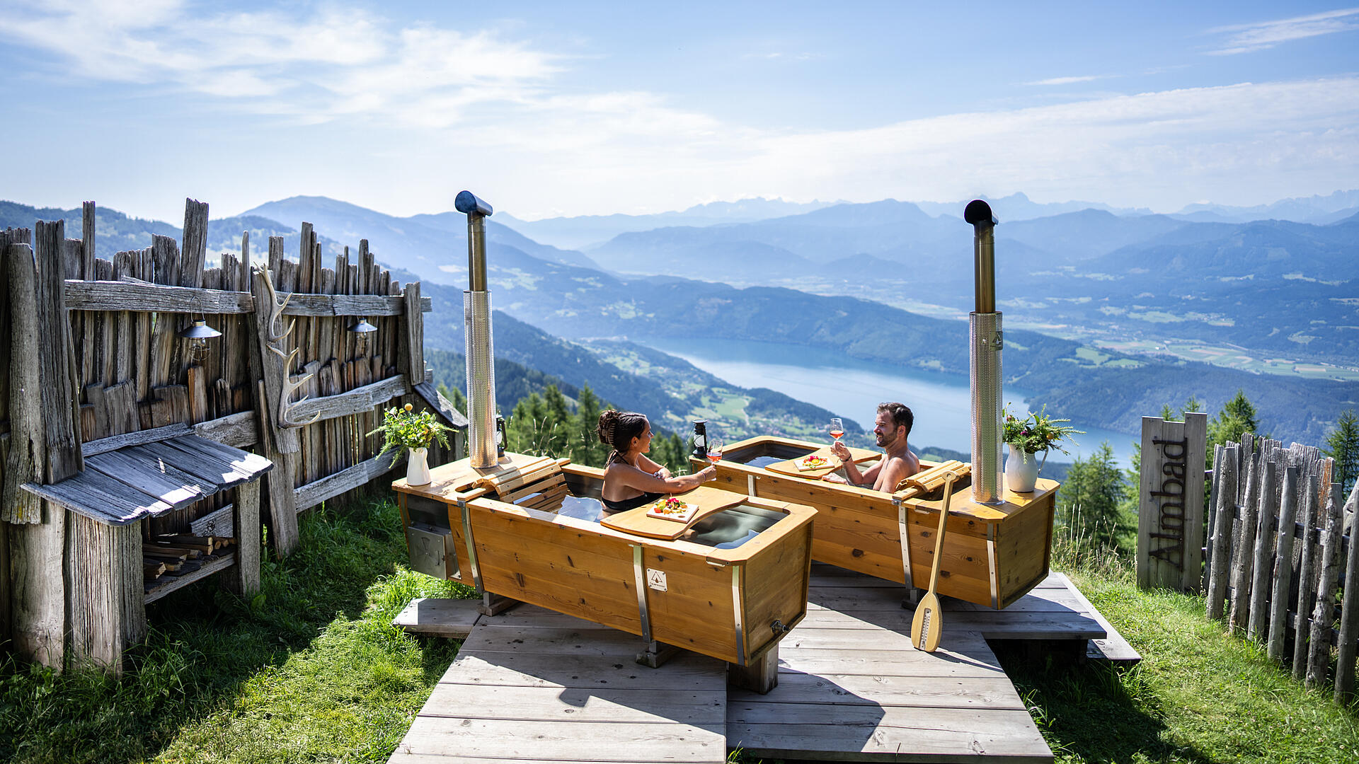 Zwei Personen genießen ein AlmBad in den Outdoorbadewannen auf der Alexanderalm, umgeben von unberührter Natur und Blick auf die Berge.