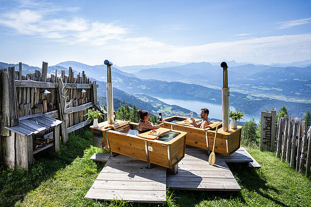 Zwei Personen genießen ein AlmBad in den Outdoorbadewannen auf der Alexanderalm, umgeben von unberührter Natur und Blick auf die Berge.