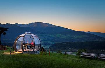 2 Personen genießen ihr Dinner in der Glaskuppel in einer Sommernacht