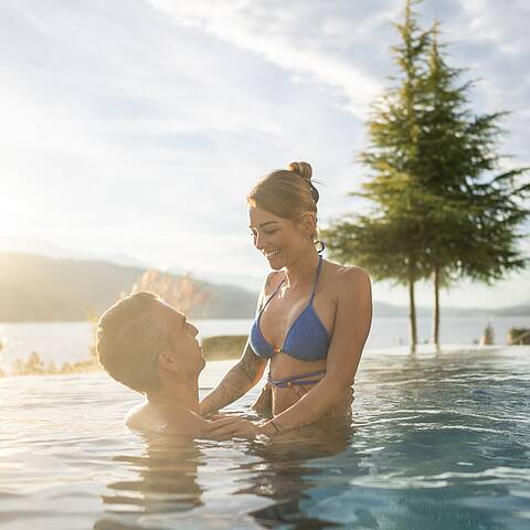 Mann hebt Frau im Außenpool des Badehauses mit Ausblick auf den Millstätter See hoch