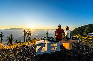 Pärchen sitzt auf Zeitbank am Goldeck und genießt den Ausblick