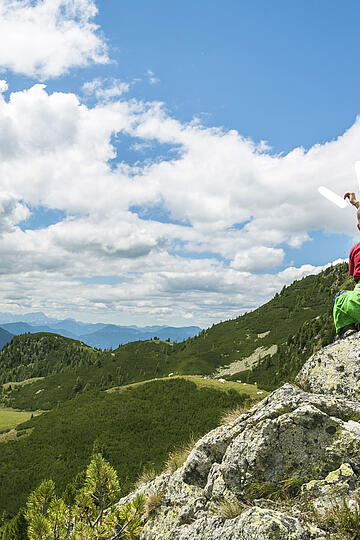 2 Kinder sitzen auf einem Felsvorsprung und betrachten das Bergpanorama der Nockberge